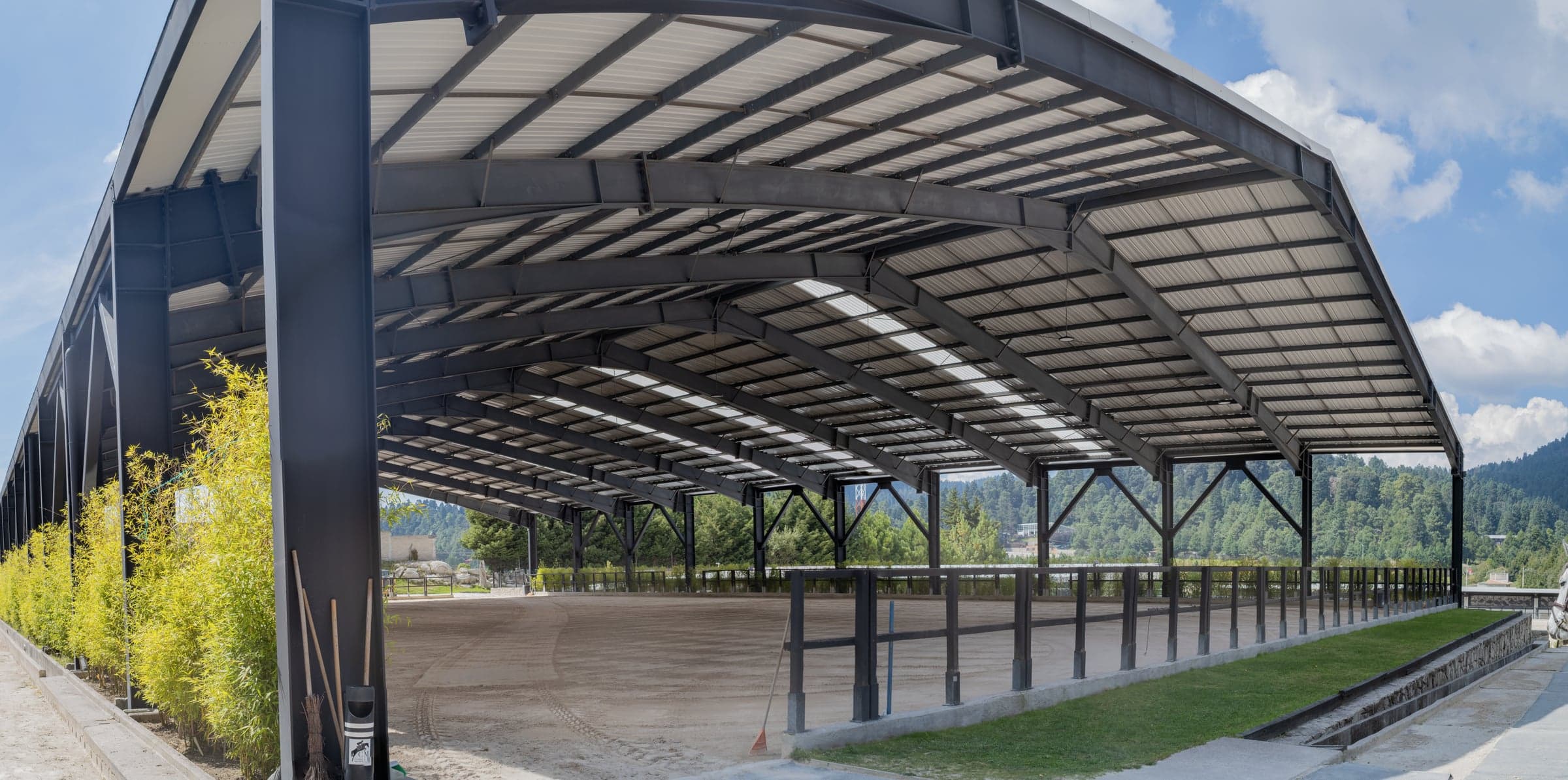 Pista techada con estructura de acero y cubierta translúcida, vacía, con bambú a lo largo de un costado.