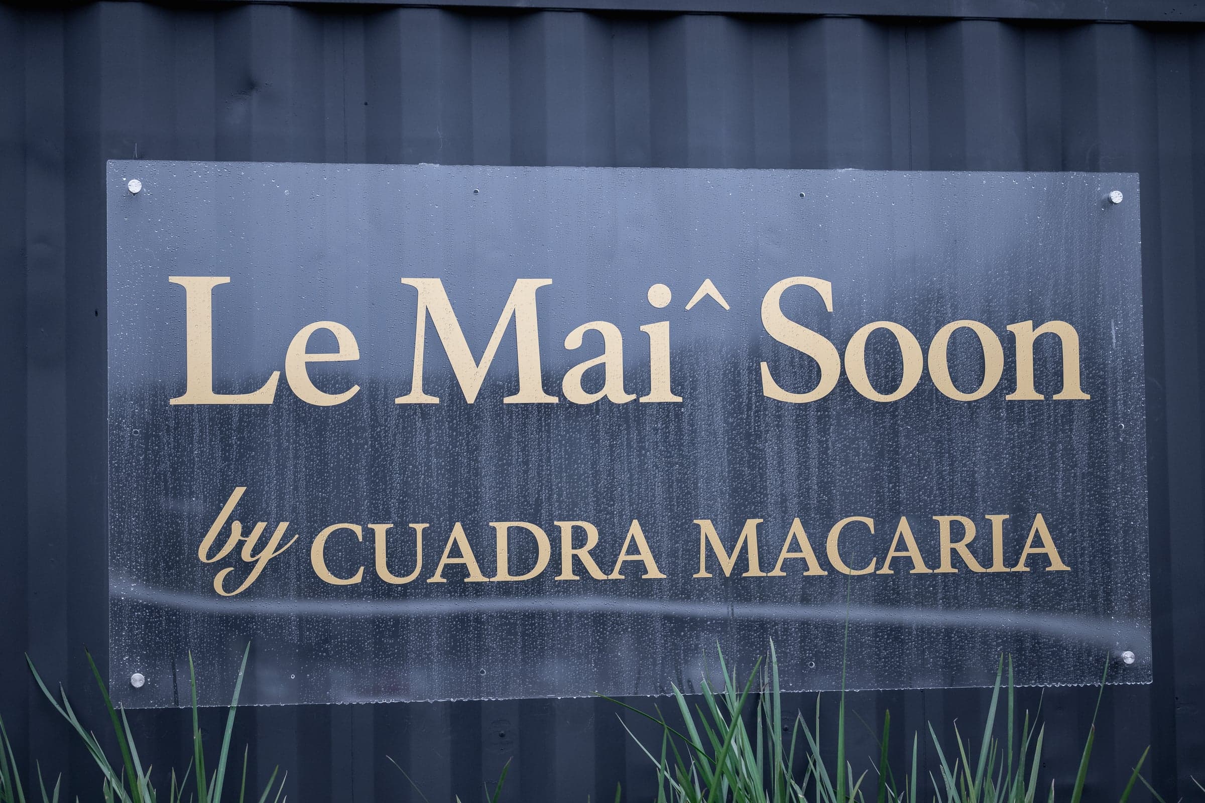 Letrero «Le Mai Soon by Cuadra Macaria» en letras doradas sobre un contenedor negro.